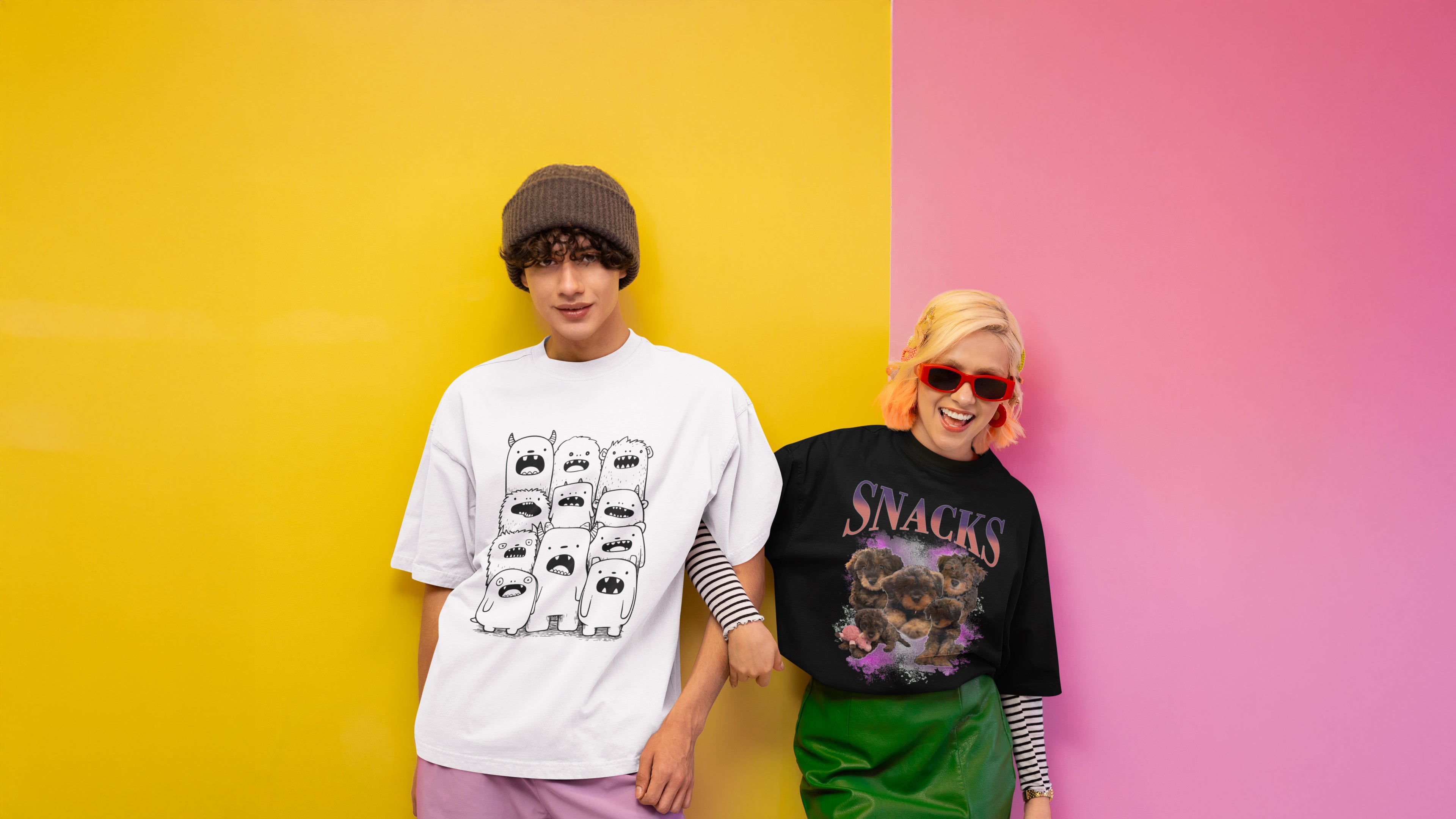 Two people standing against a colorful background, one wearing a white t-shirt with graphic design and the other wearing a black t-shirt with 'SNACKS' text.