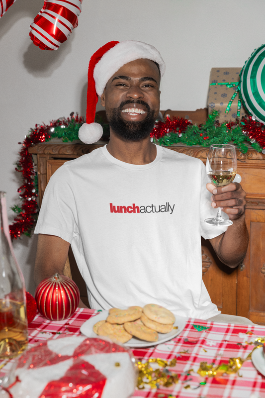 Man wearing a Santa hat and 'lunch actually' shirt at a festive table with cookies and wine.